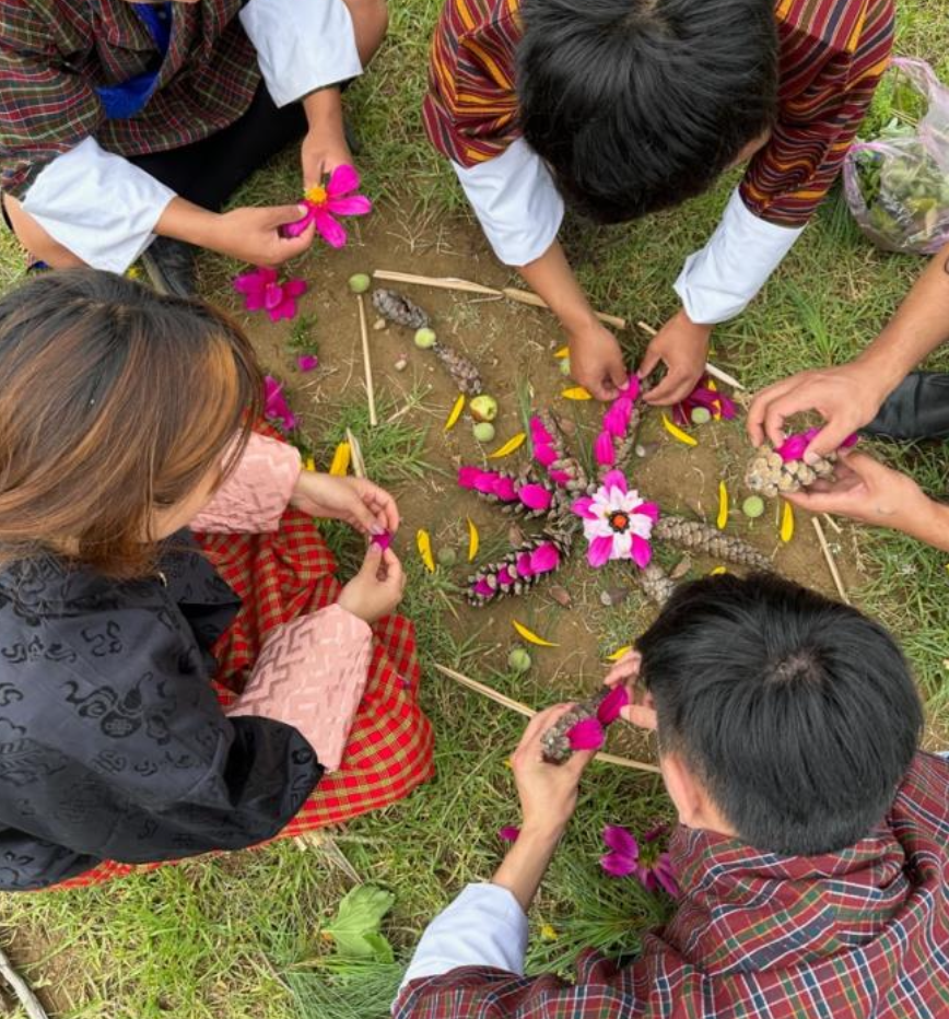 Students arranging flowers, pine cones and sticks into a mandala on the ground