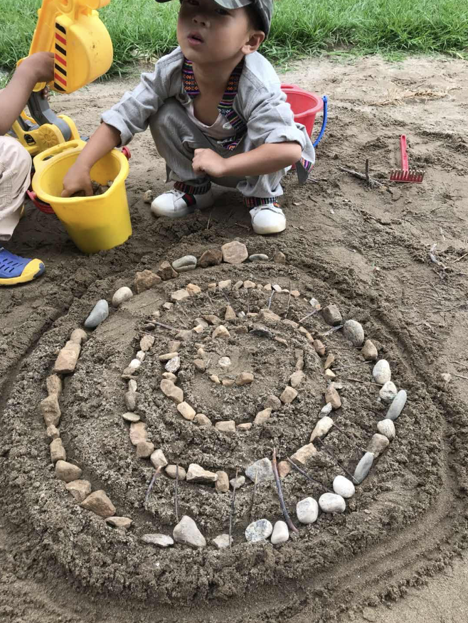 A child arranging stones and sticks into a spiral in the sand