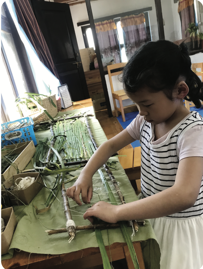 A child weaving with fresh grass and twigs on a handmade loom