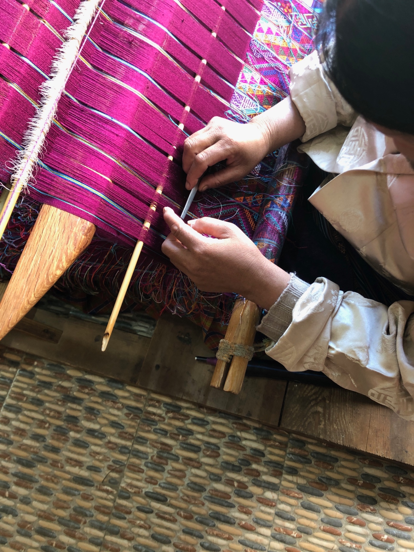 A weaver's hands working magenta threads on a traditional Bhutanese loom